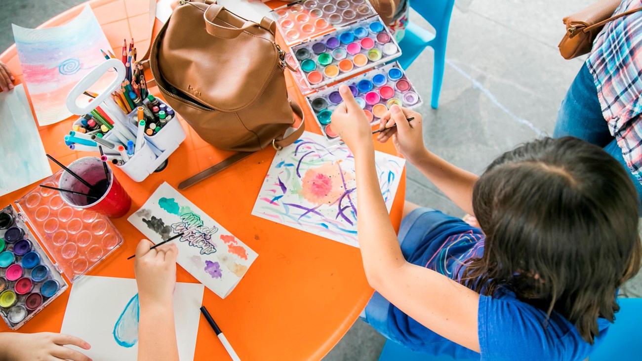a child sitting at a craft table working on watercolors