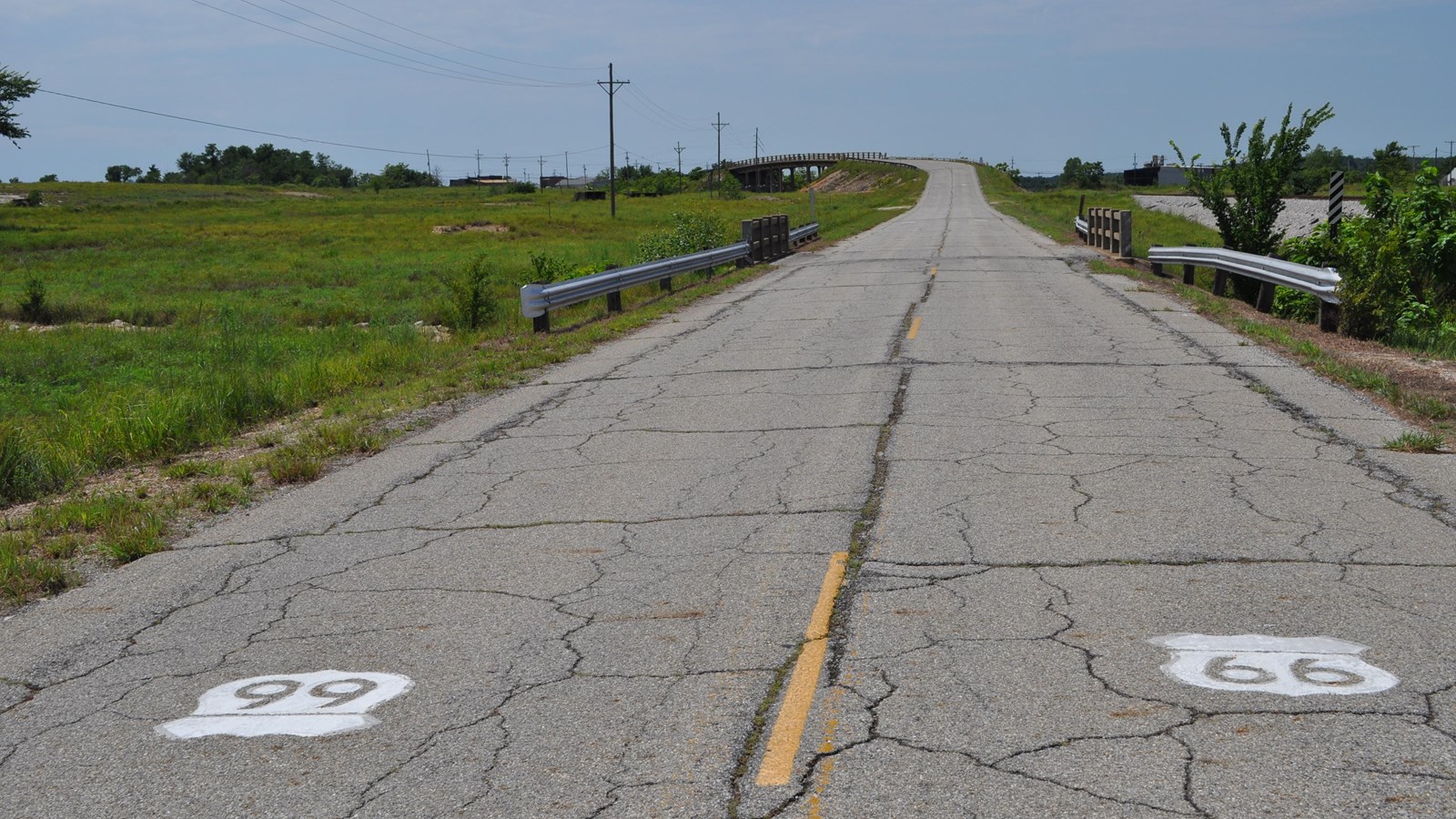 Two lane, asphalt road leading to bridge structure. Route 66 shields painted on pavement.