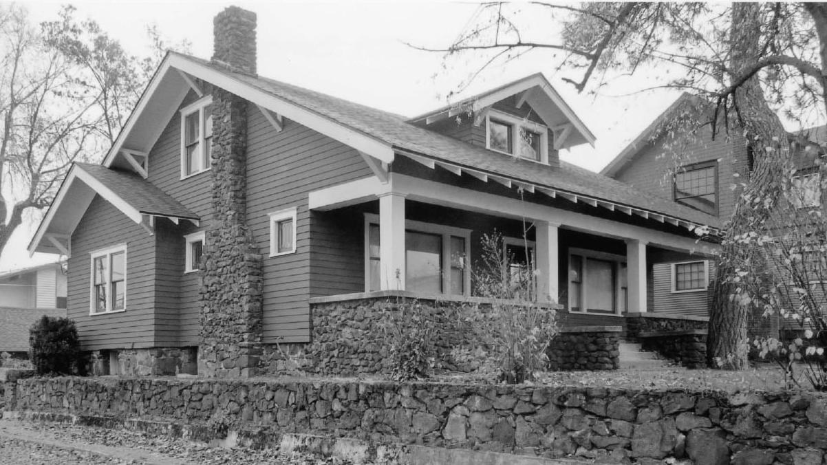 Black and white brick house with a porch, chimney, and stone fence
