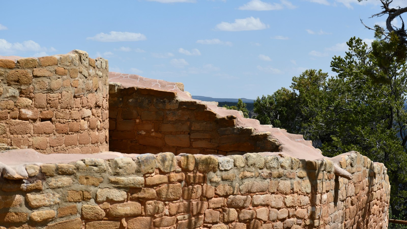 Sandstone masonry walls lie in the shade of trees with a distant canyon view.