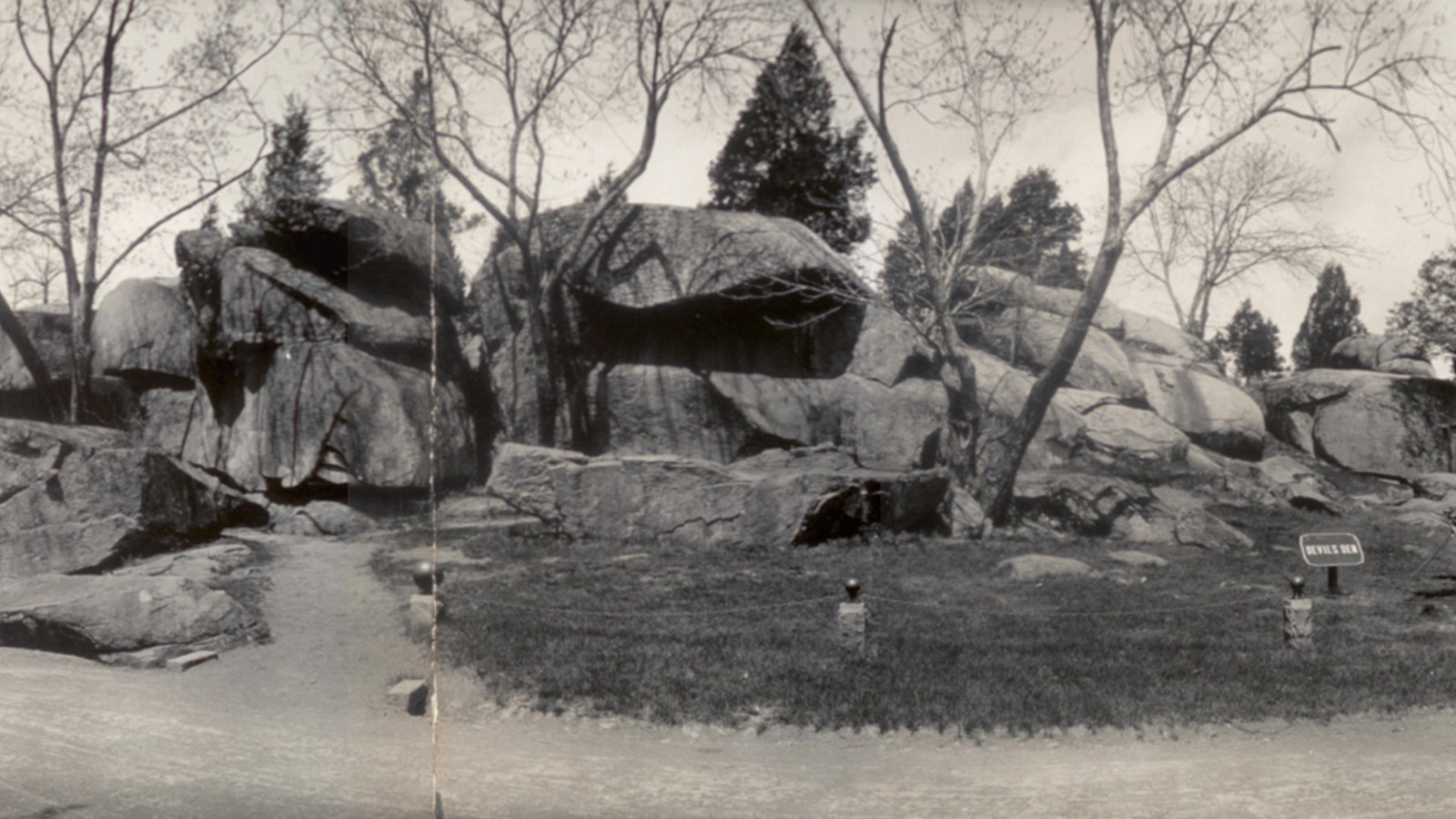 Historical photo of a rock formation with large boulders next to a road.