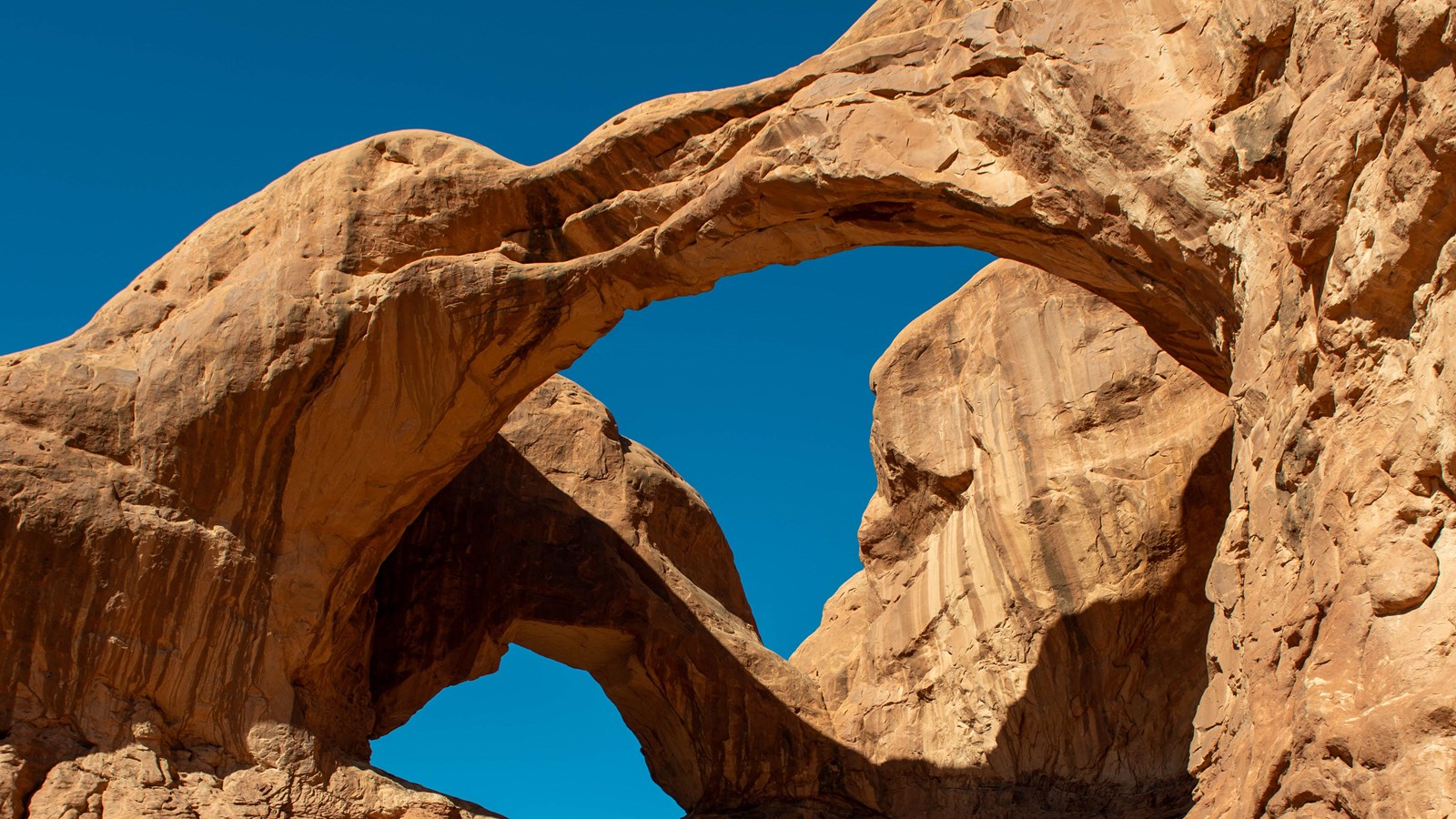 Two sandstone arches connected on the left against a backdrop of blue sky. 