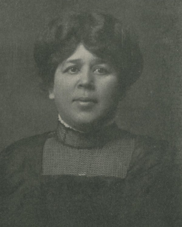 Black and white photograph of woman in high-necked black dress and close-styled hair.