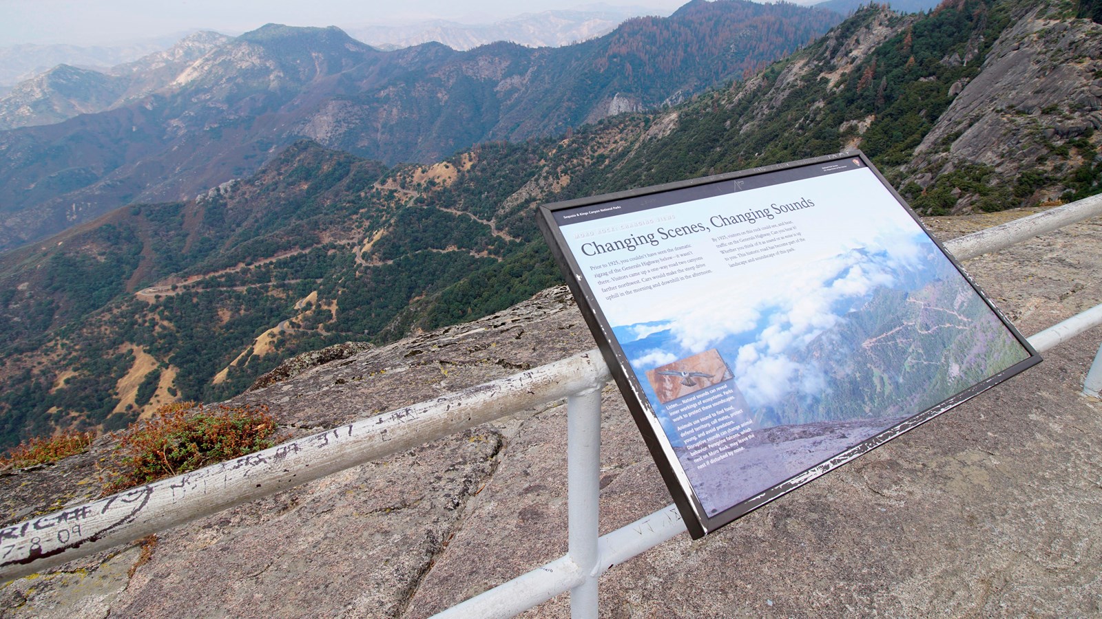 A metal panel sits high upon a rock with views stretching many miles