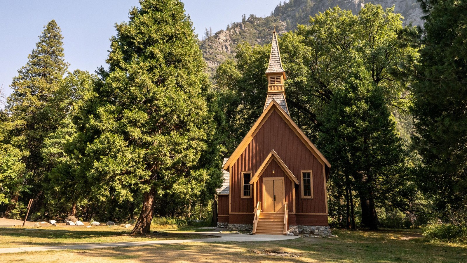 A simple, red-brown building with a steeply pitched roof and a steeple
