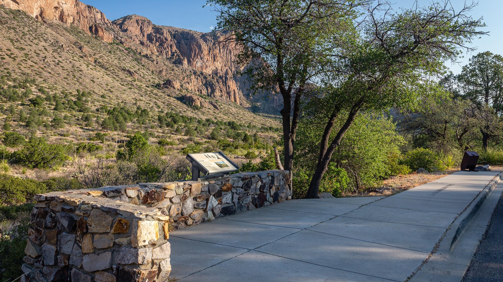 a small paved area with an information panel and a view of a mountain valley