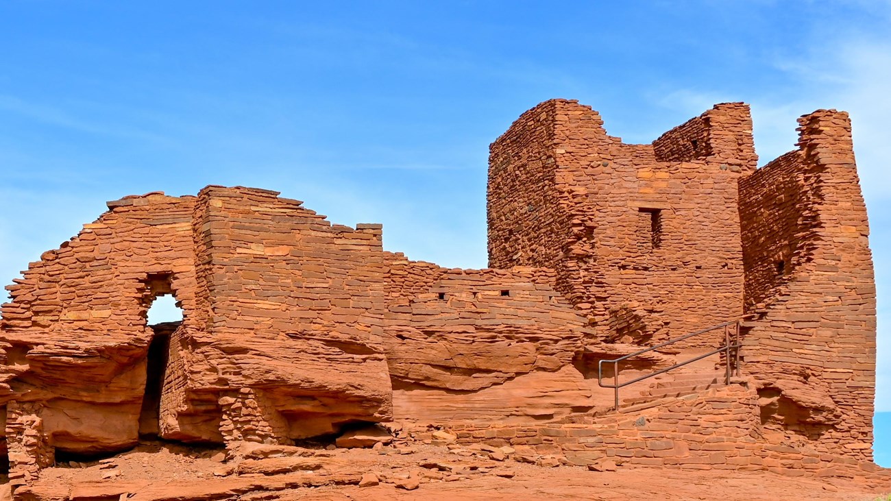 A red sandstone pueblo with a tower and three story tall wall 