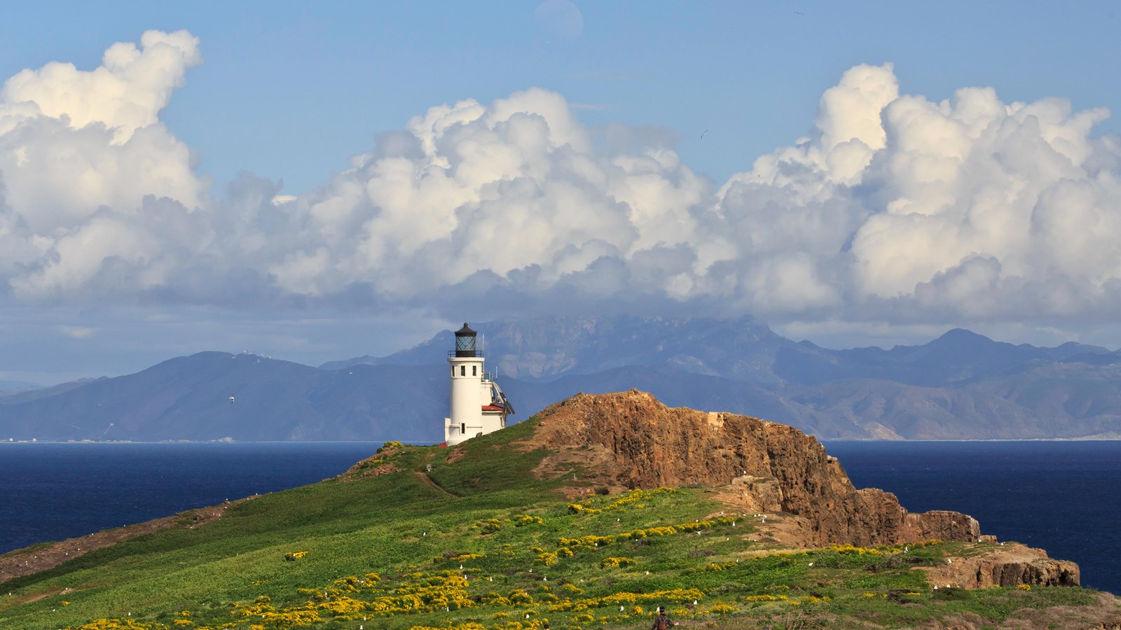 Lighthouse near cliff with ocean and clouds.