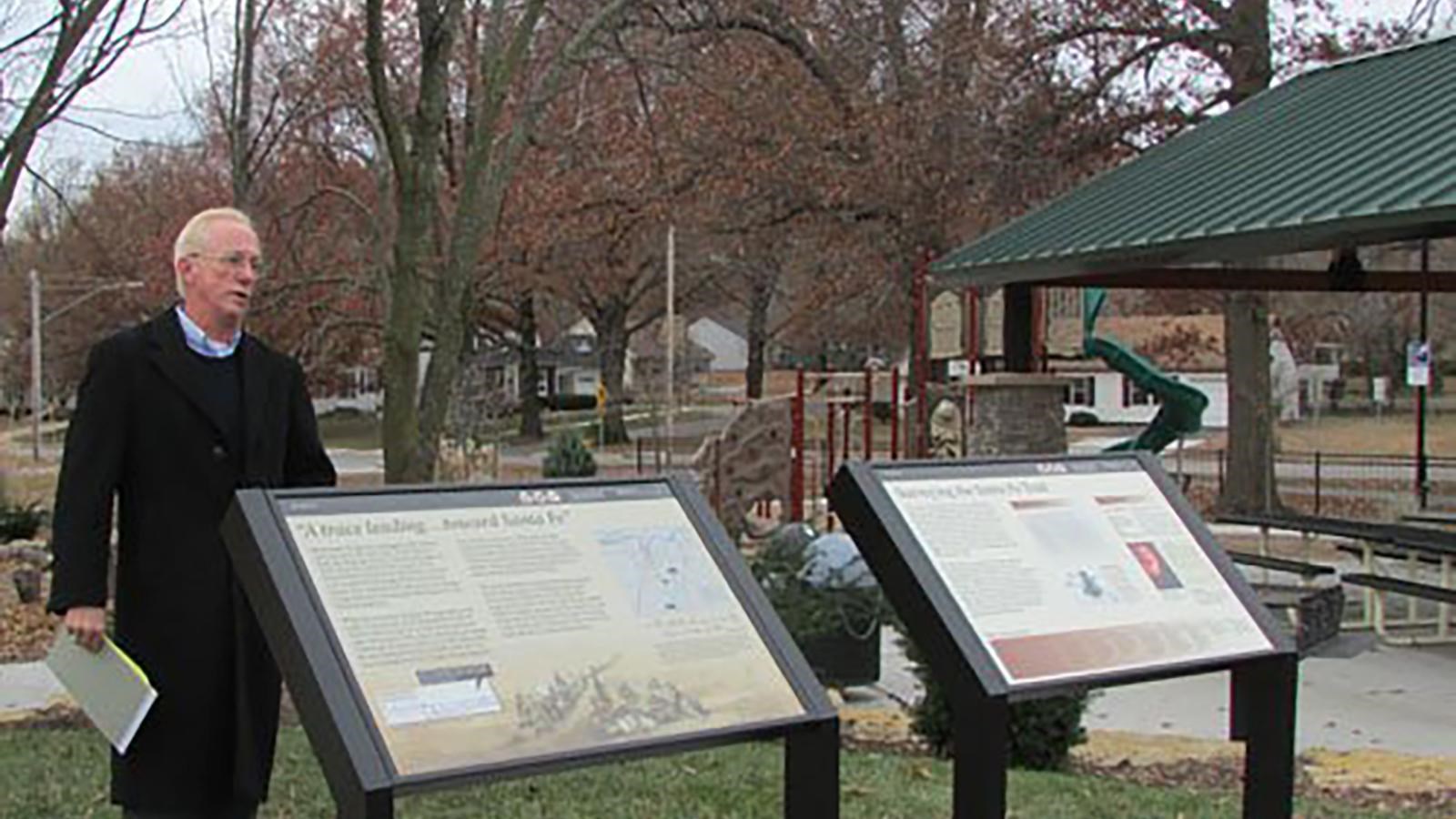 A man stands behind two wayside exhibits in a city park.