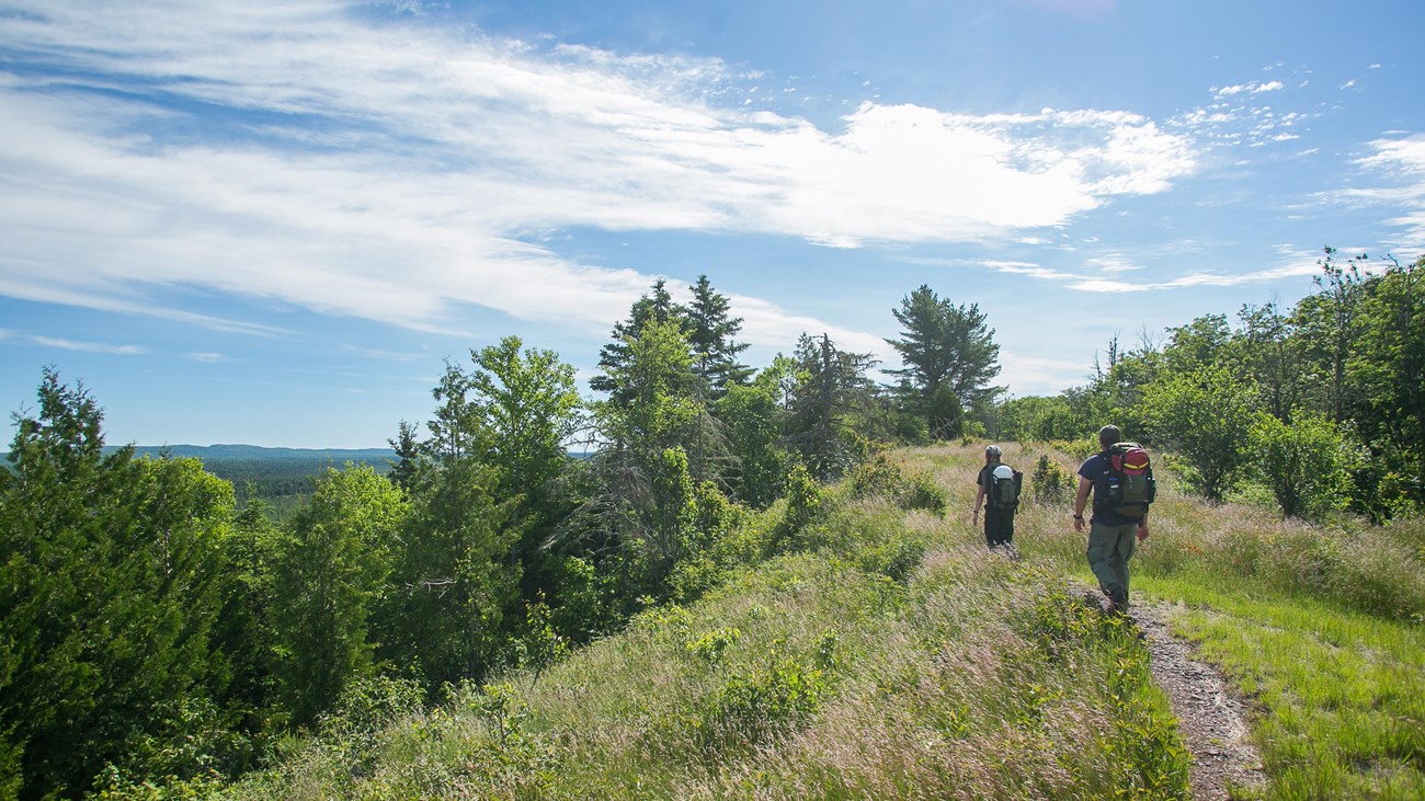 Two people with backpacks hike along a ridge top trail