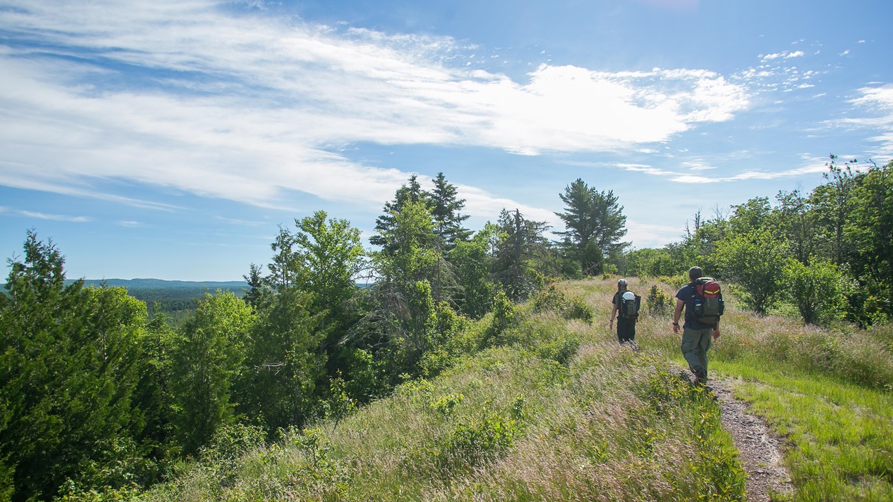 Two people with backpacks hike along a ridge top trail 