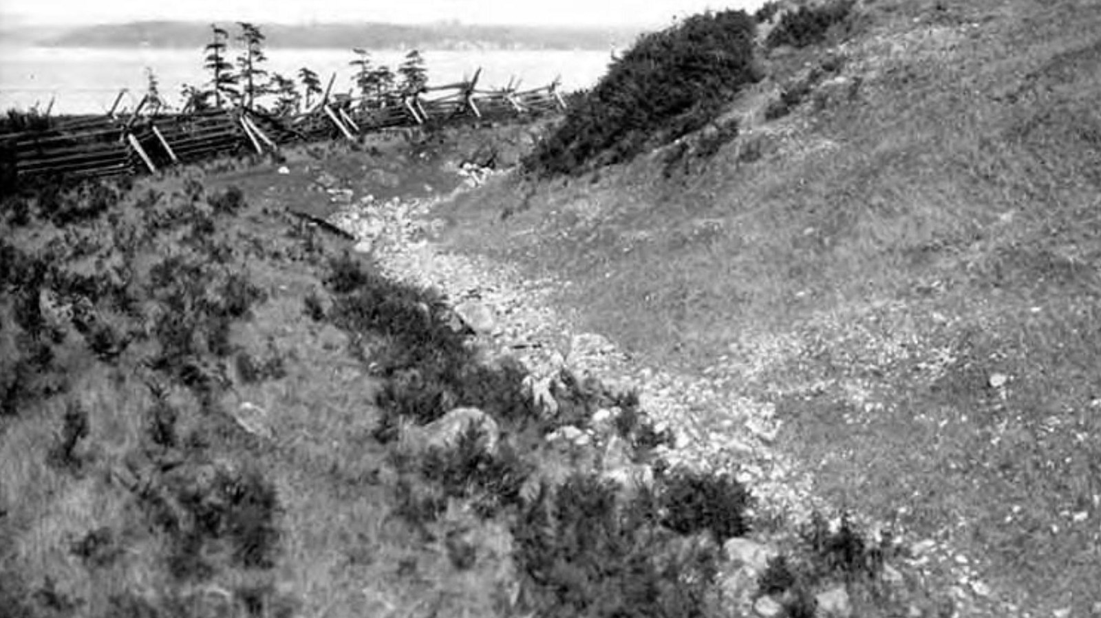 Black and white photo of a fence beside a slope