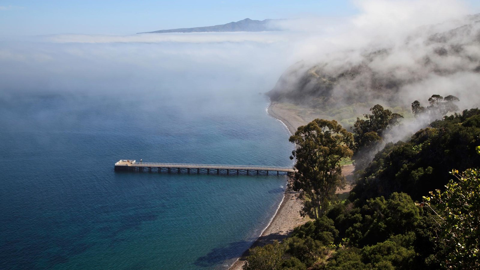 Island coastline with pier, fog and mountains in the background.