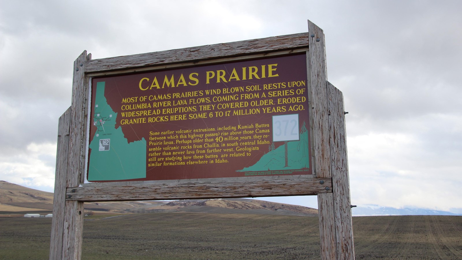 A large wooden sign for Camas Prairie with an open field behind it