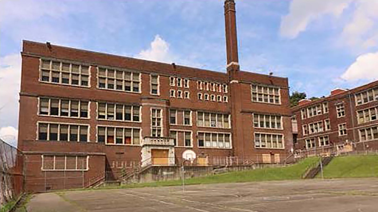 3-story red brick school building with basketball court in front. 