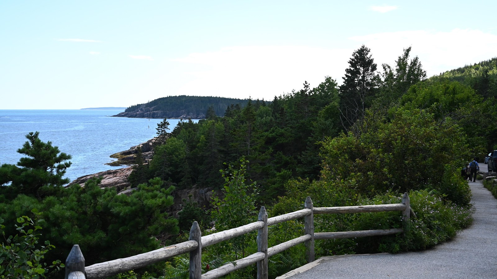 Gravel path with wooden railings next to sprawling greenery and view of the ocean.