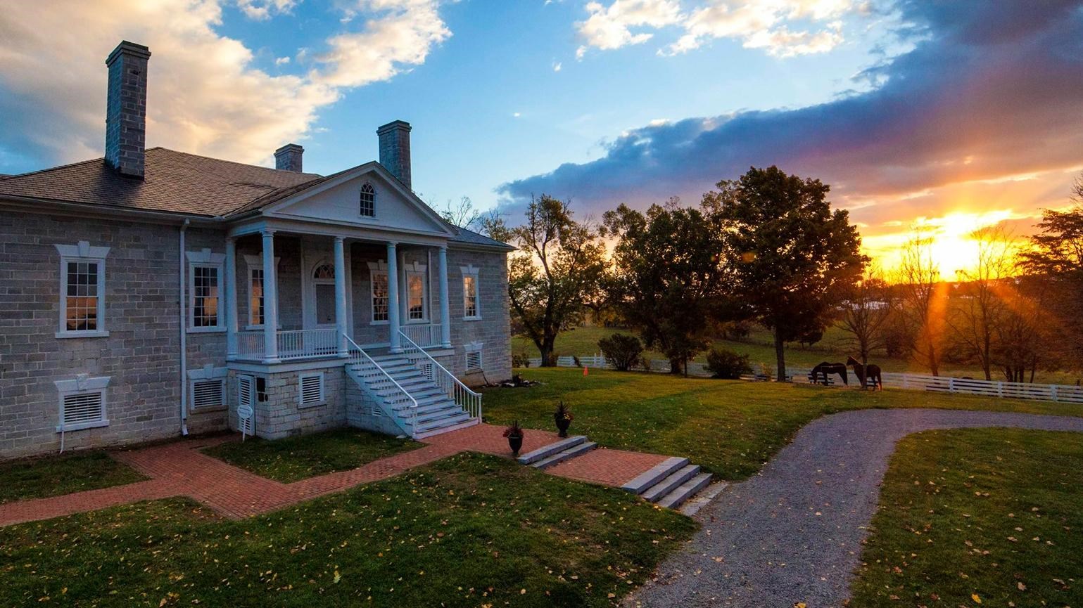 Sunrise lights the clouds over a limestone antebellum mansion.