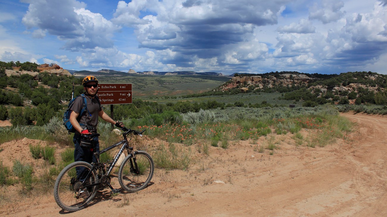 A man stands with a bike along a dirt road
