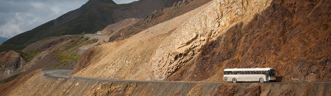 a bus driving on a dirt road on the side of a mountain