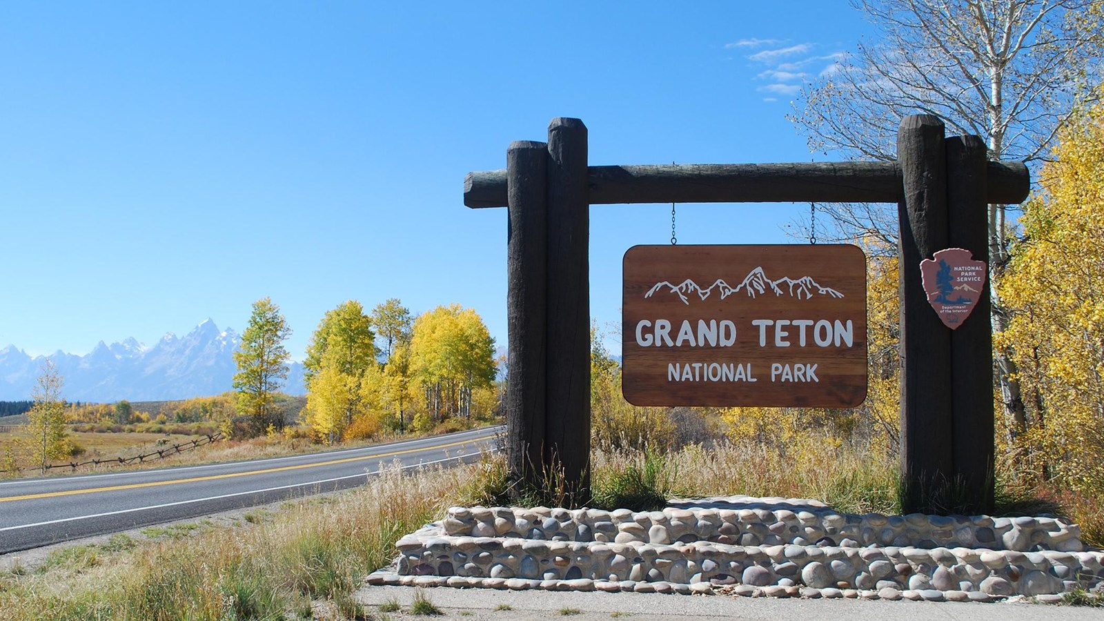 Large wooden grand teton national park sign at a turnout with mountains in the distance. 