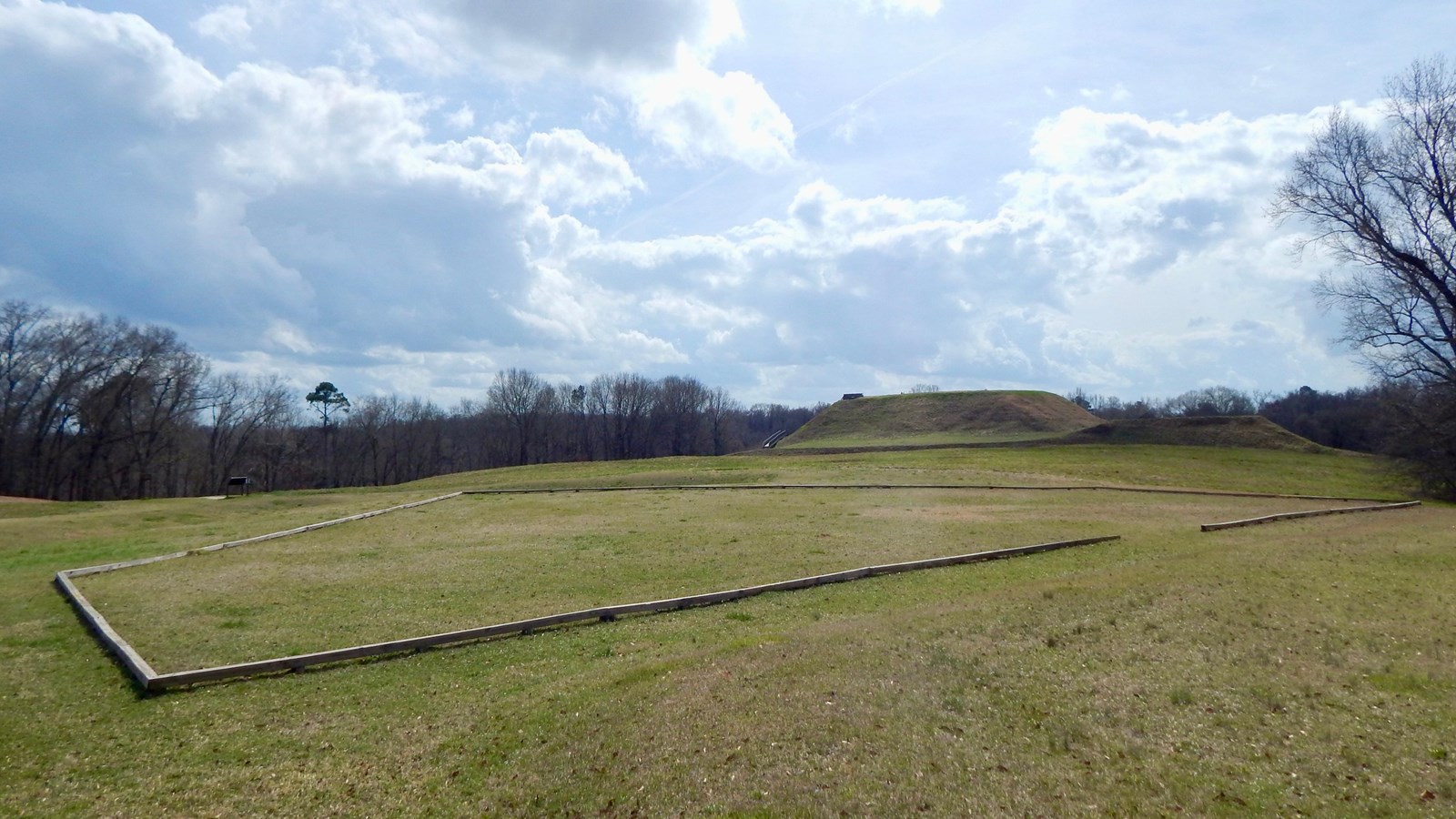 A wooden outline of the foundation of the trading post in a grassy field.