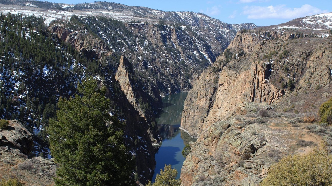 A deep steep canyon with a narrow body of water running far below. Snow is dusted on the canyon rim