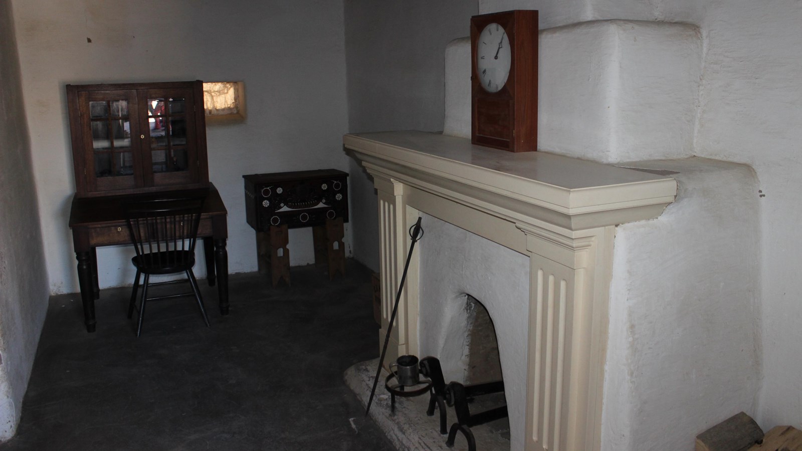 A sparse office in a whitewashed room. A fireplace dominates one side.