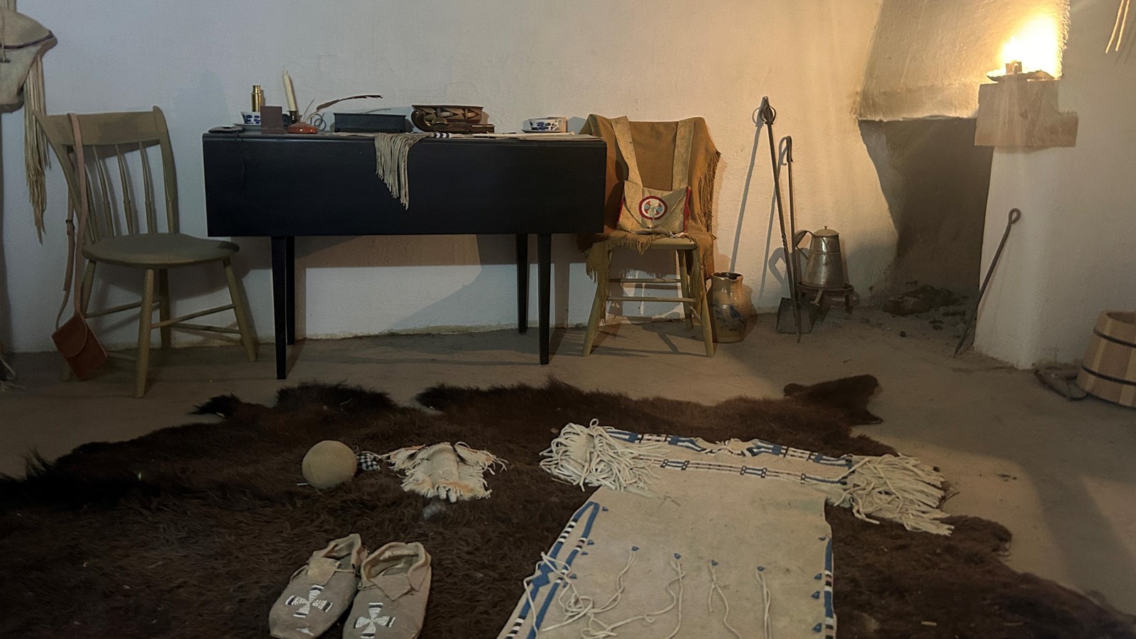 CHeyenne clothes and items are arranged on a bison robe in a sparely furnished room.