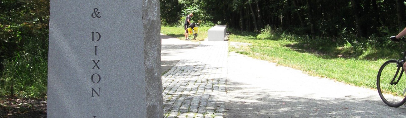 a granite obelisk next to a ten-foot wide crushed stone pathway