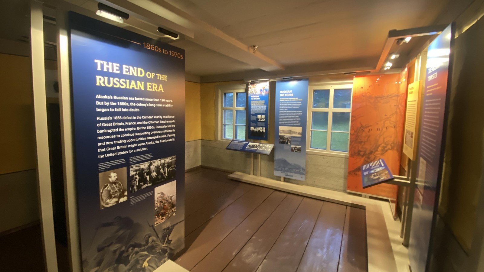 Yellow and grey walls, red floors, exhibits along two walls and middle of room, windows on one wall