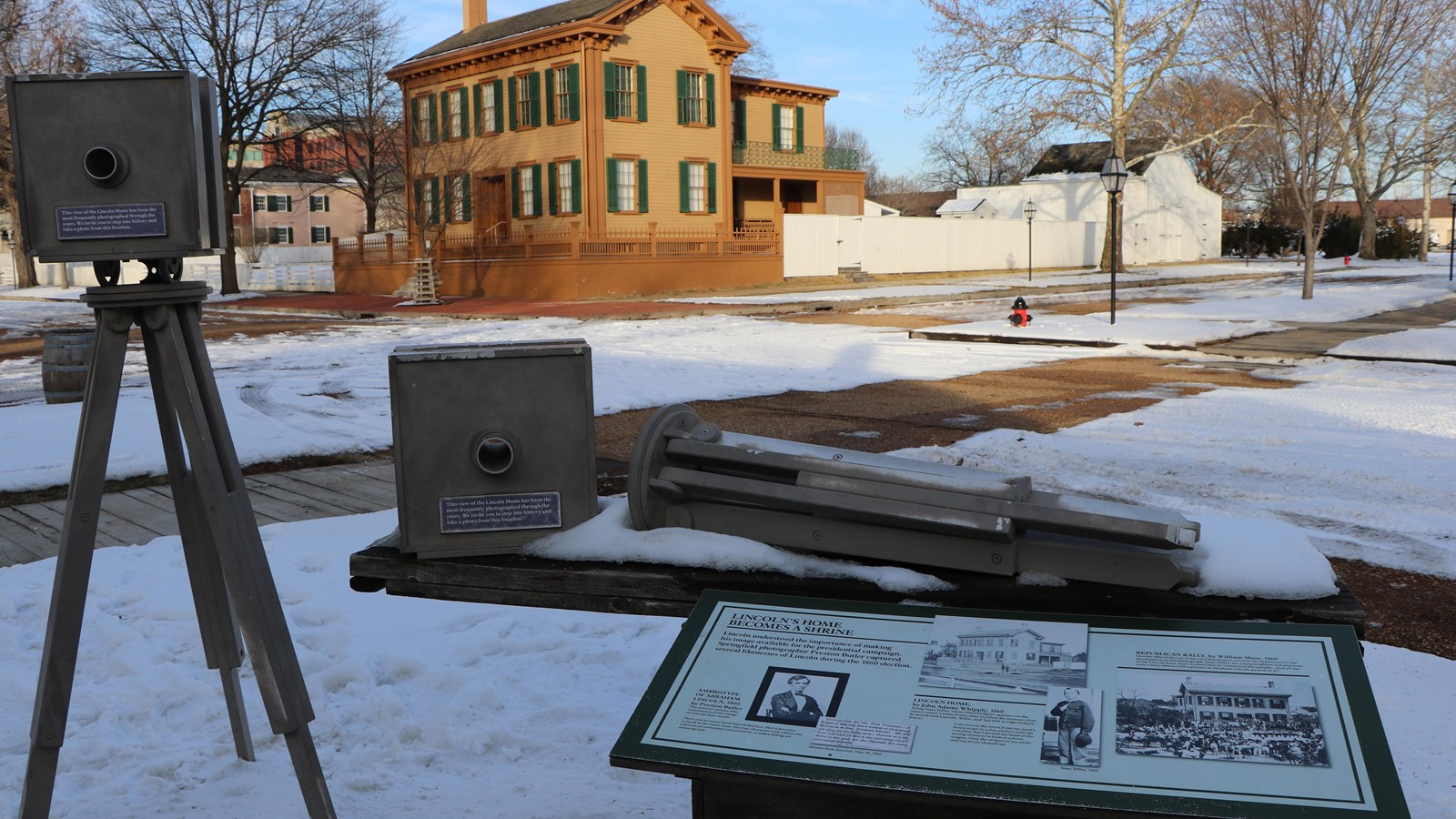 Outdoor wayside exhibit next to replica old fashioned camera with Lincoln Home in background