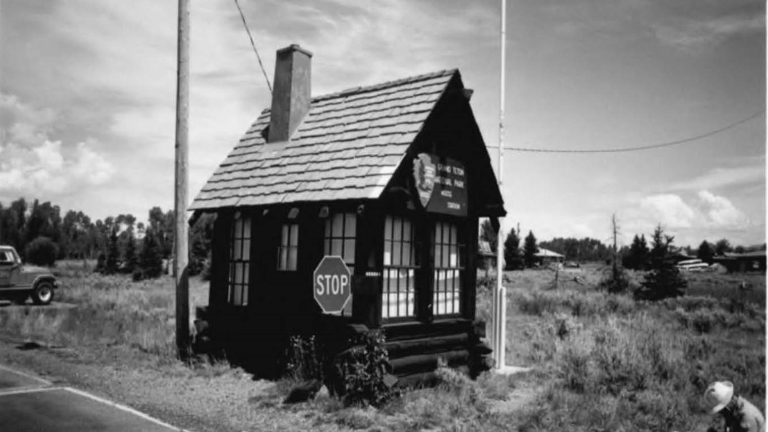 A historic black and white photo shows a small log building-the park\'s first entrance station.