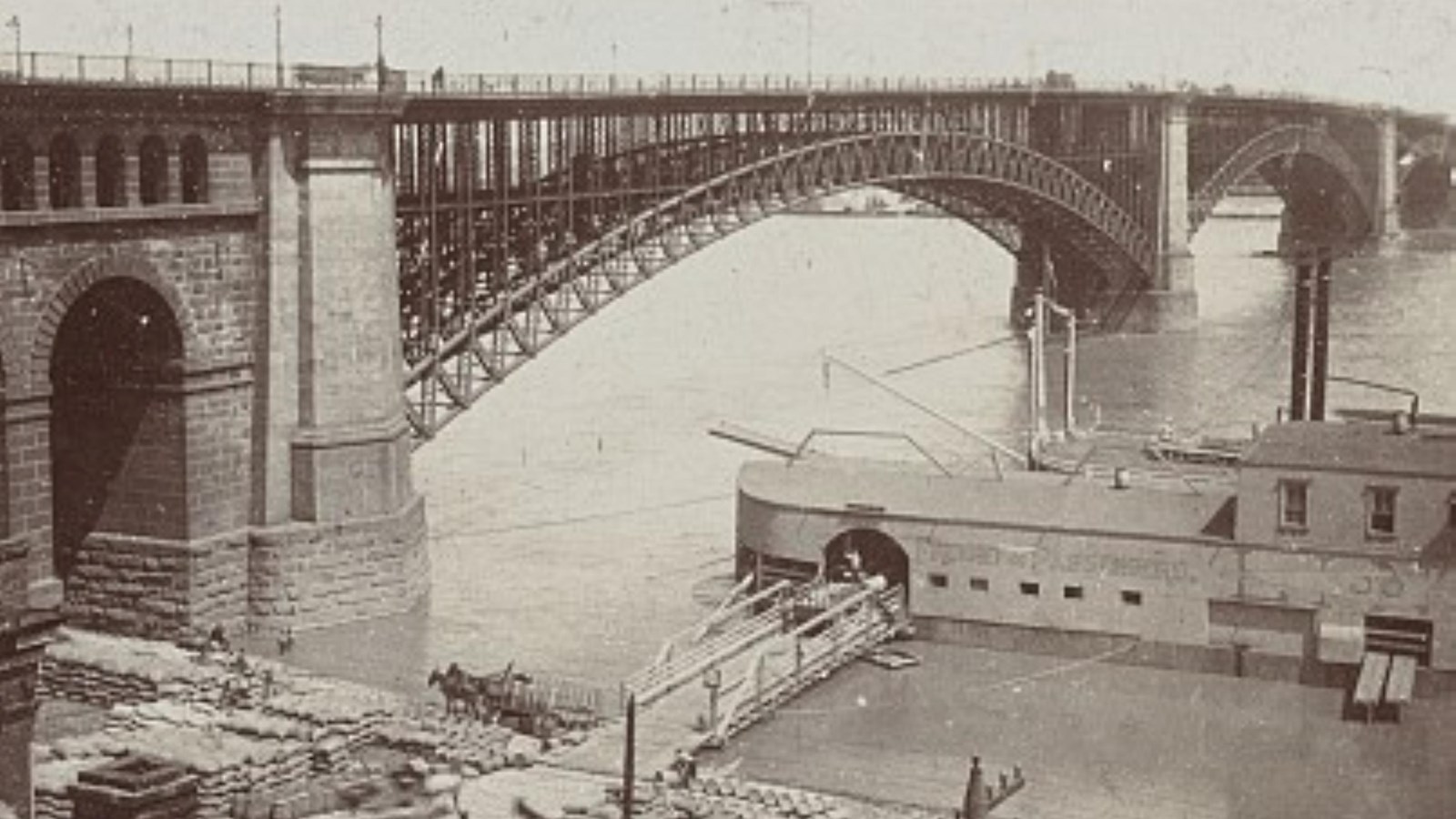 and old black and white photo of the Eads bridge with a boat and materials to be loaded stacked