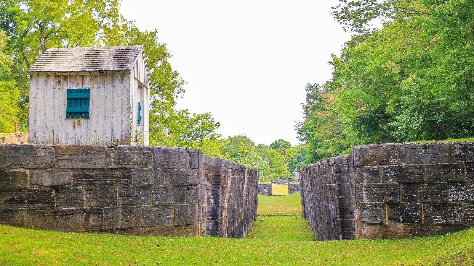 A look through a lock to another lock in the distance. A small white building sits on the left side.