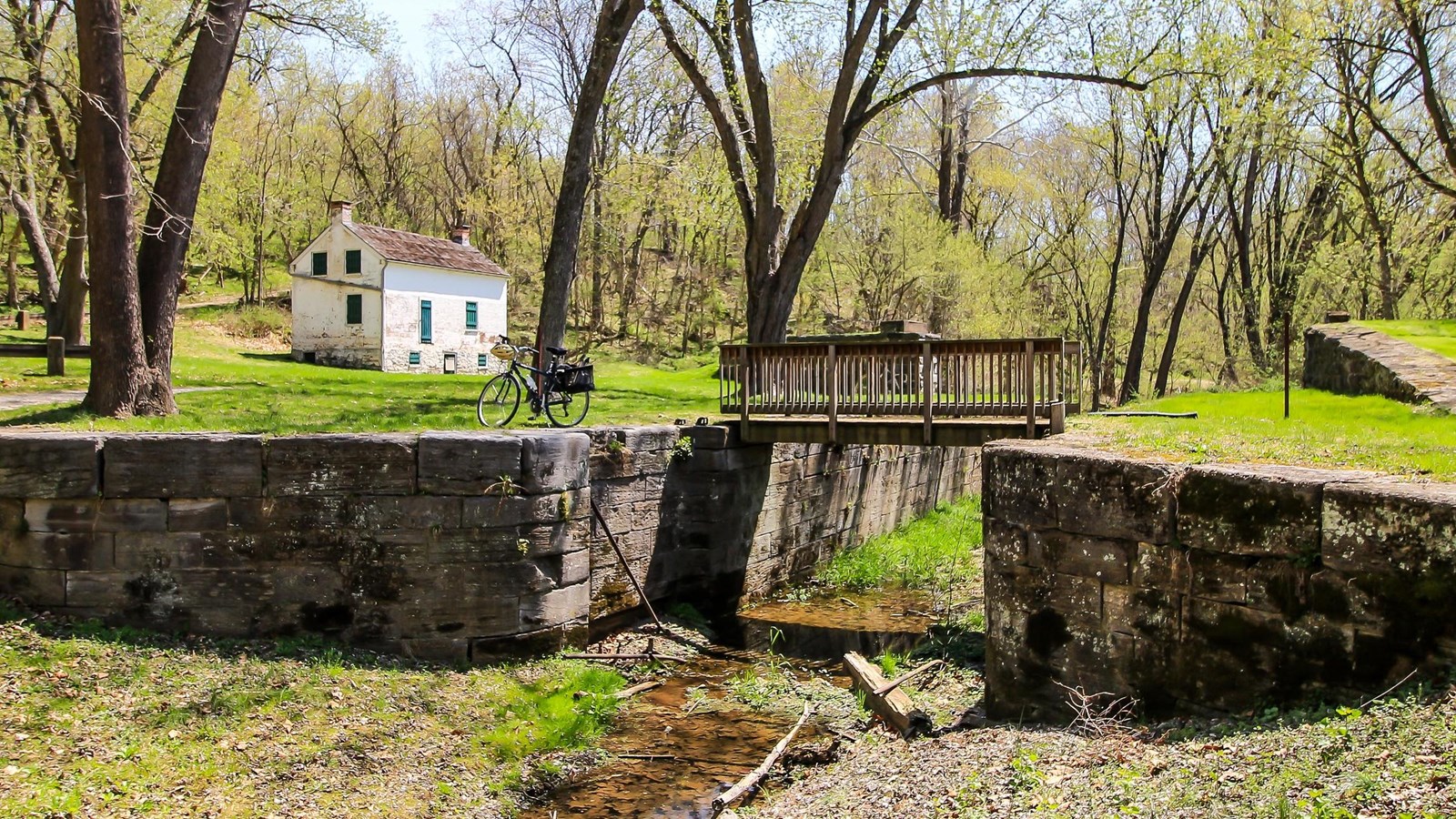 A foot bridge spans the top of a lock with a white lockhouse in the background.