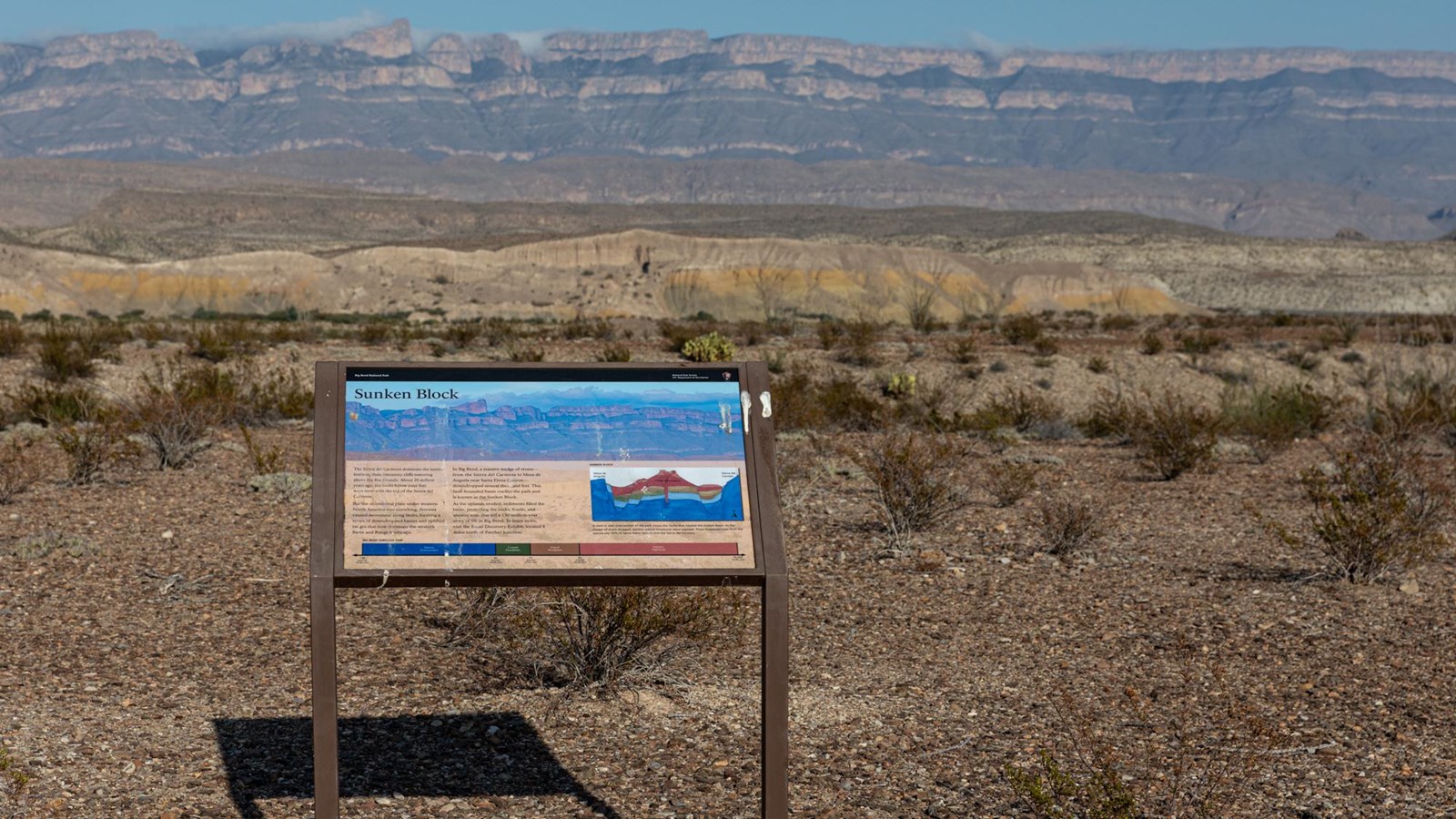 A metal sign stands in the desert, with the Sierra del Carmen rising up in the background.