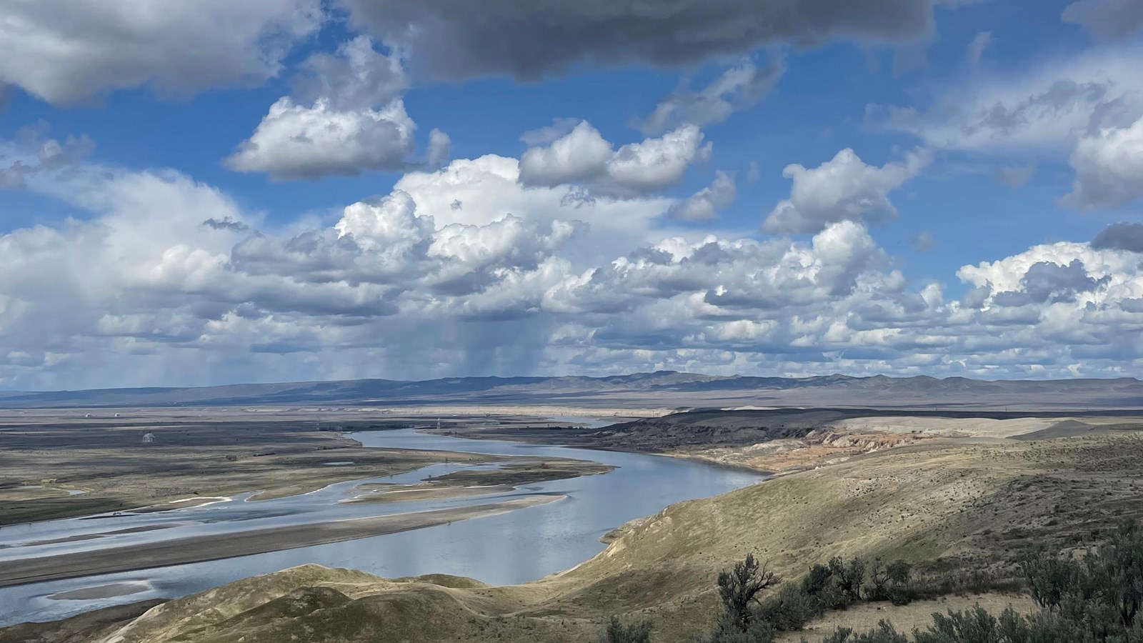 Light beige cliffs exposed along a meandering river under puffy white clouds in a blue sky