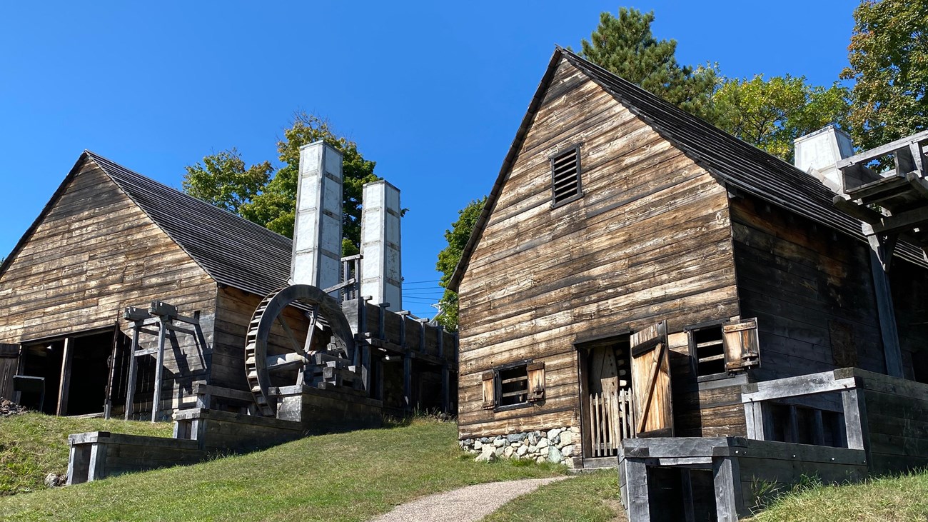 two wood-sided buildings with chimneys and water wheels under a bright blue sky