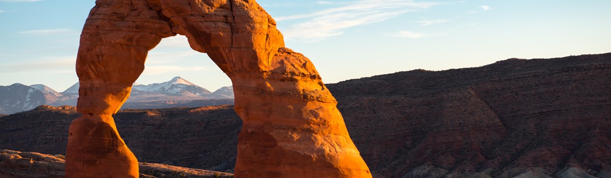 a stone arch glowing orange in the sun with mountains in the distance