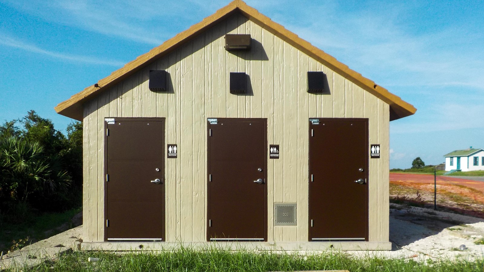A tan and brown restroom building stands on green grass.