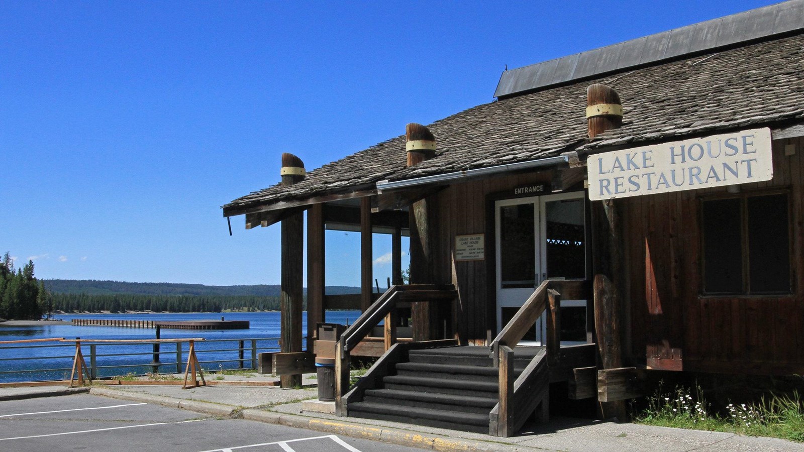 A wooden building with columns that look like piers sits next to a lake.