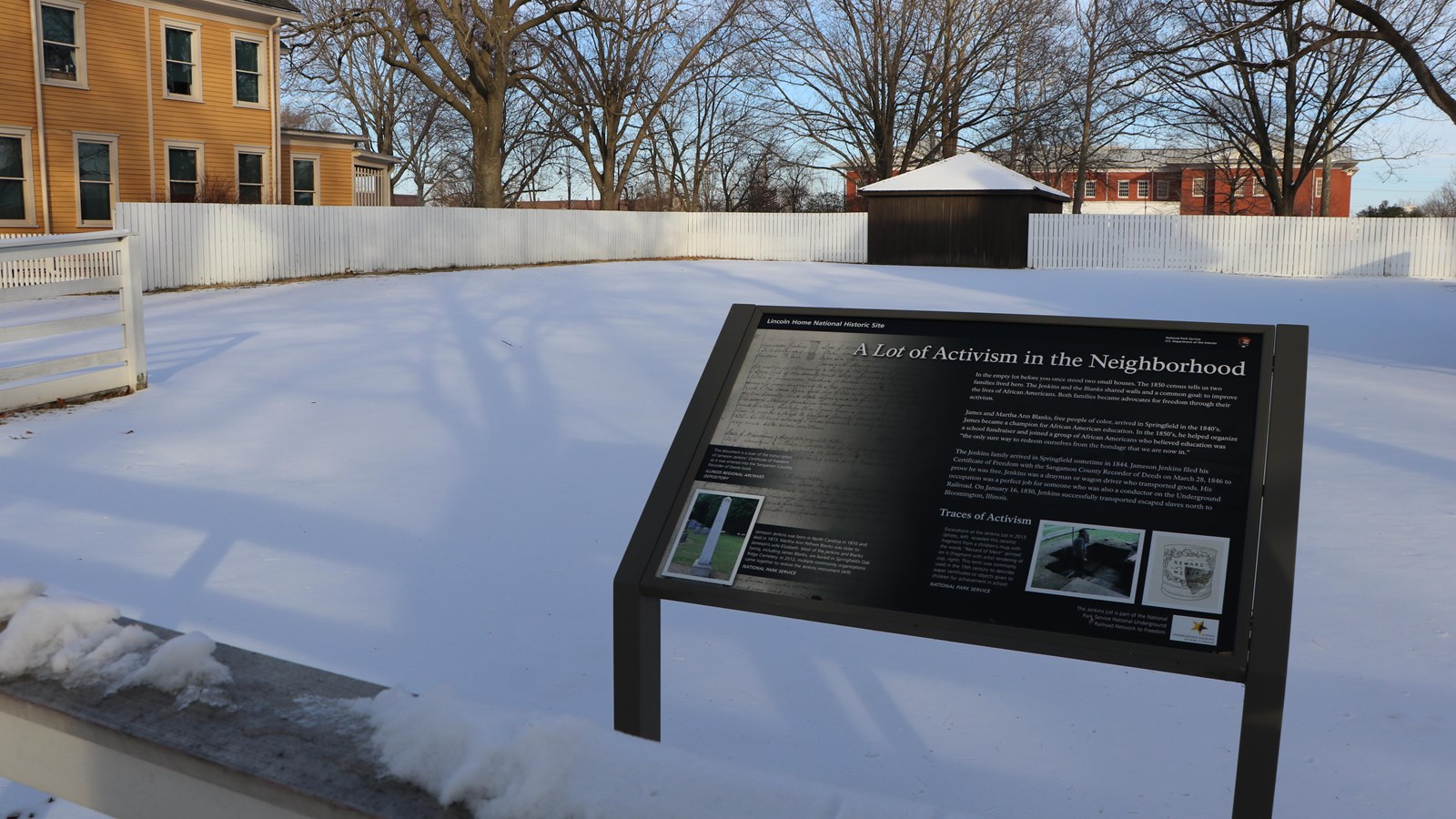 Outdoor wayside Exhibit located in empty property lot, surrounded by wooden fence