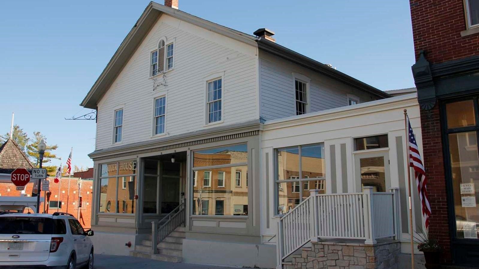 A white, two story wood frame building has two storefront windows and a light green trim.