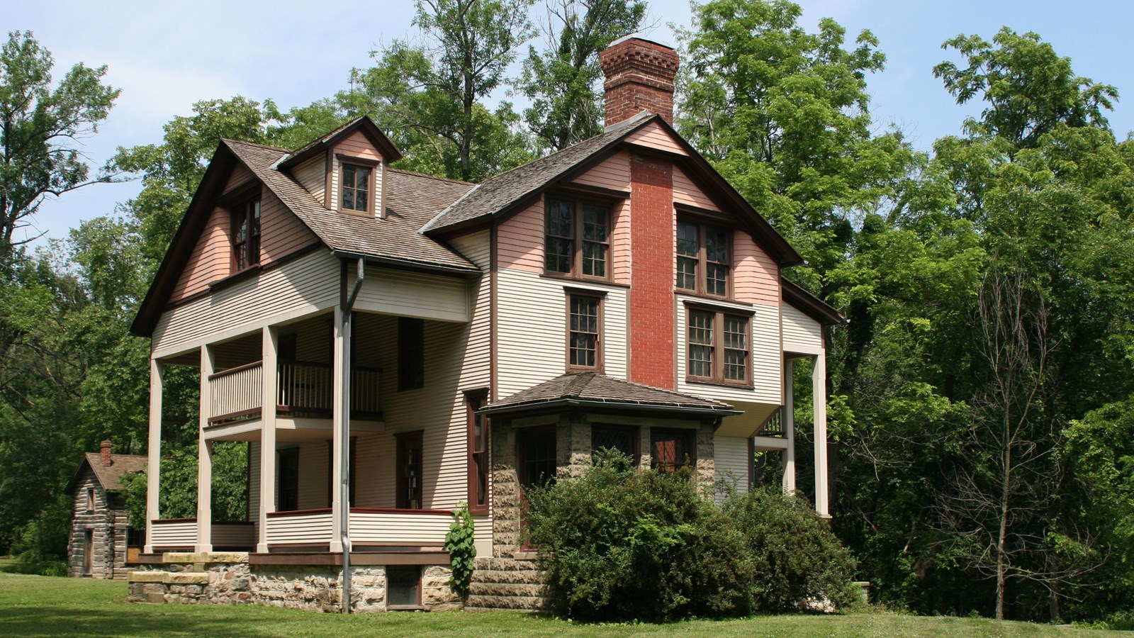 Building made of wood painted white and pink, stone, and red brick in a manicured field.  