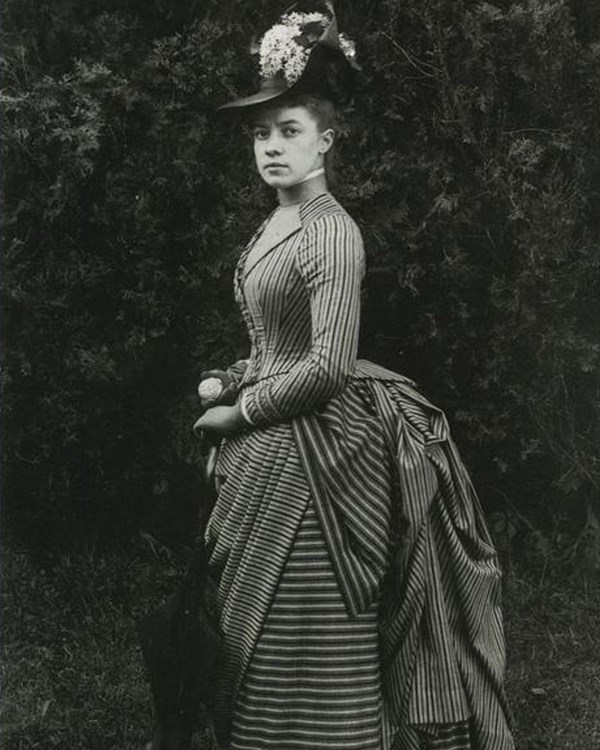 Black and white photograph of Alice Austen as a young woman. She is wearing a striped dress.