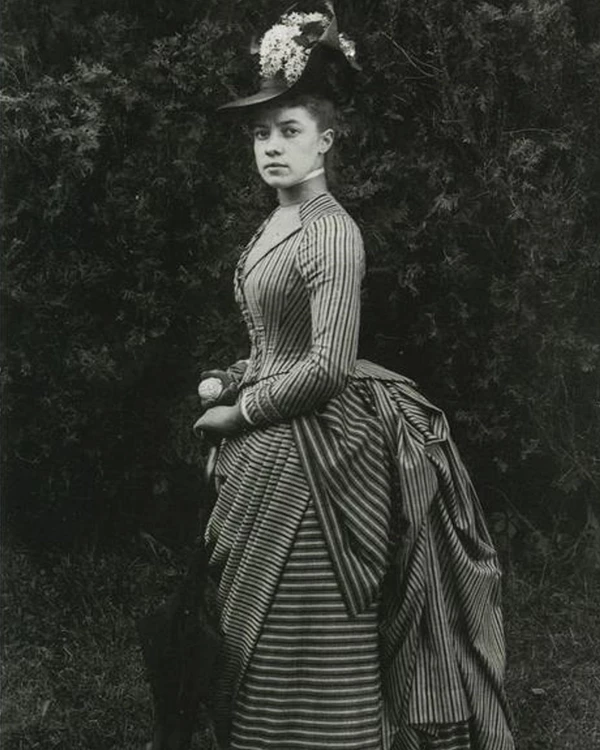 Black and white photograph of Alice Austen as a young woman. She is wearing a striped dress.