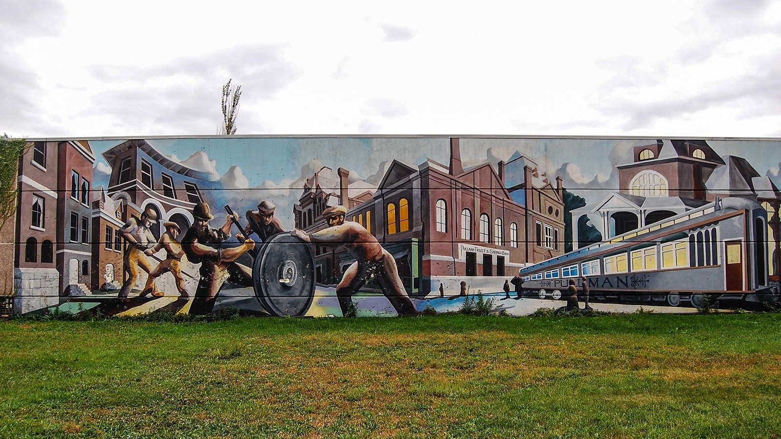 A mural on the backside of a building depicting workers, historic buildings, and trains.