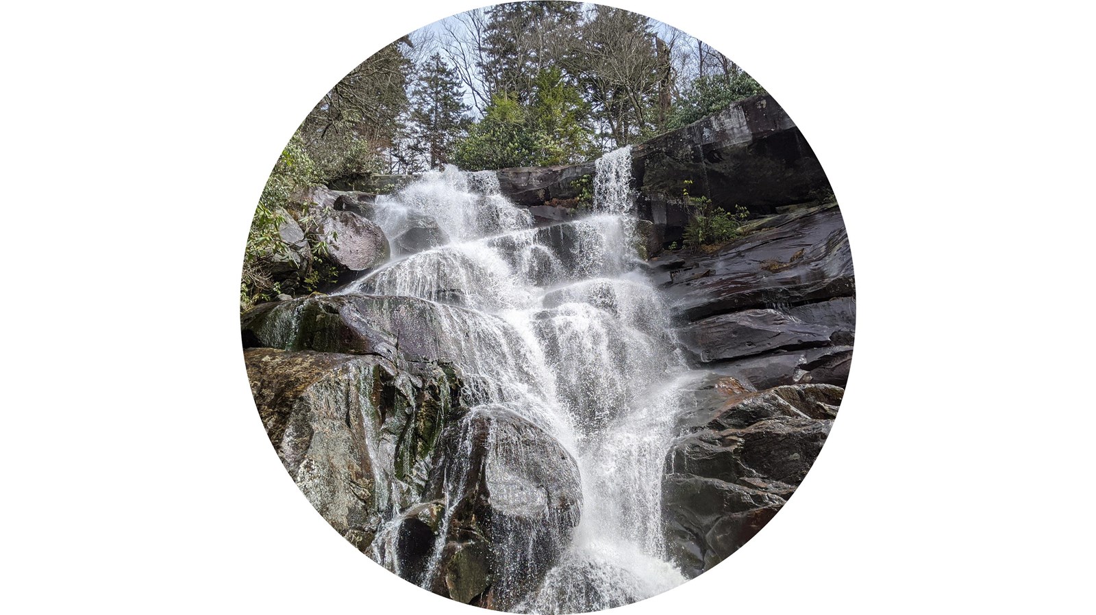 A waterfall flowing in many tiers down large boulders. Falls is framed by vegetation.