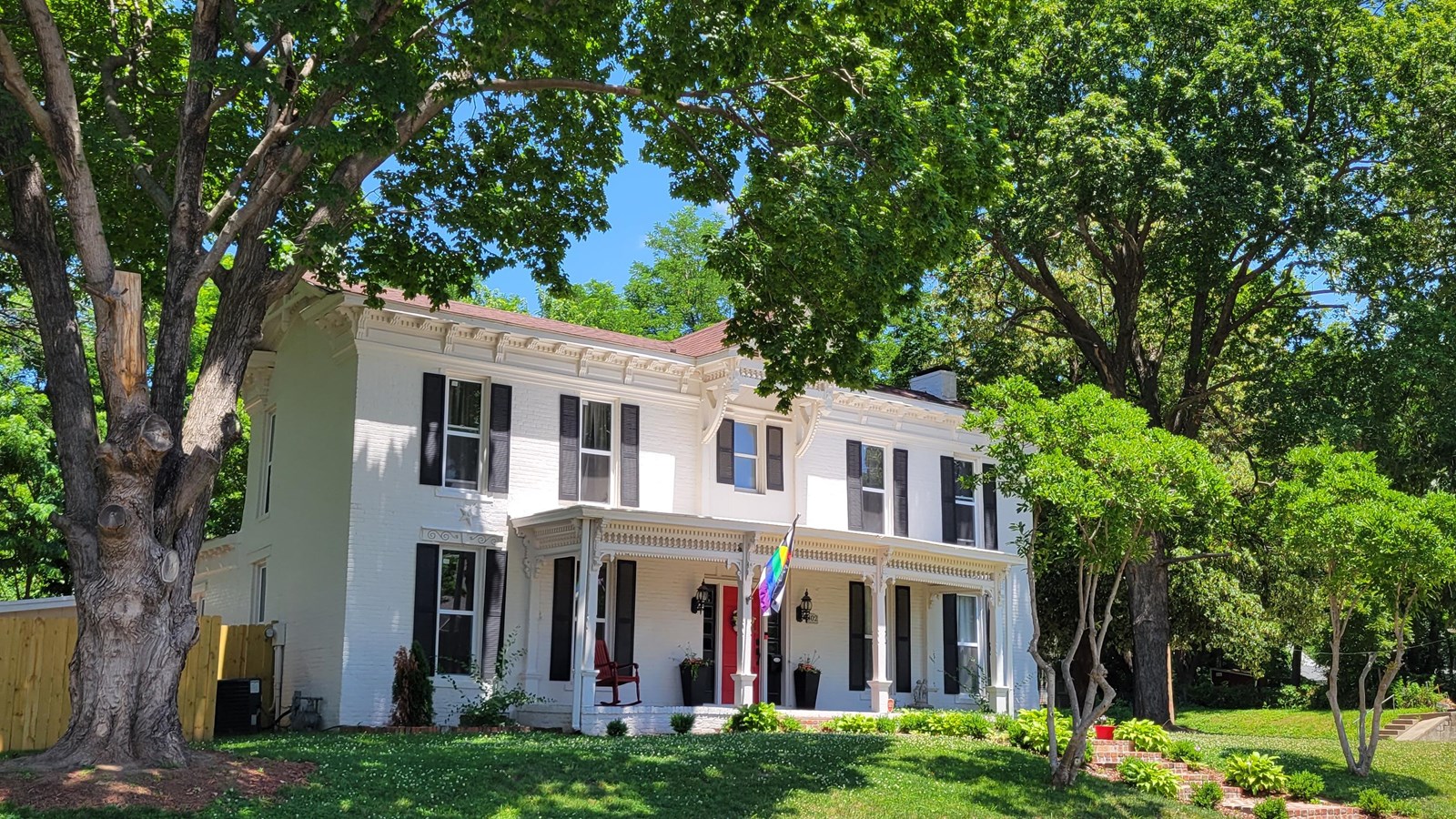 Large, white, two-story colonial home between two large trees.