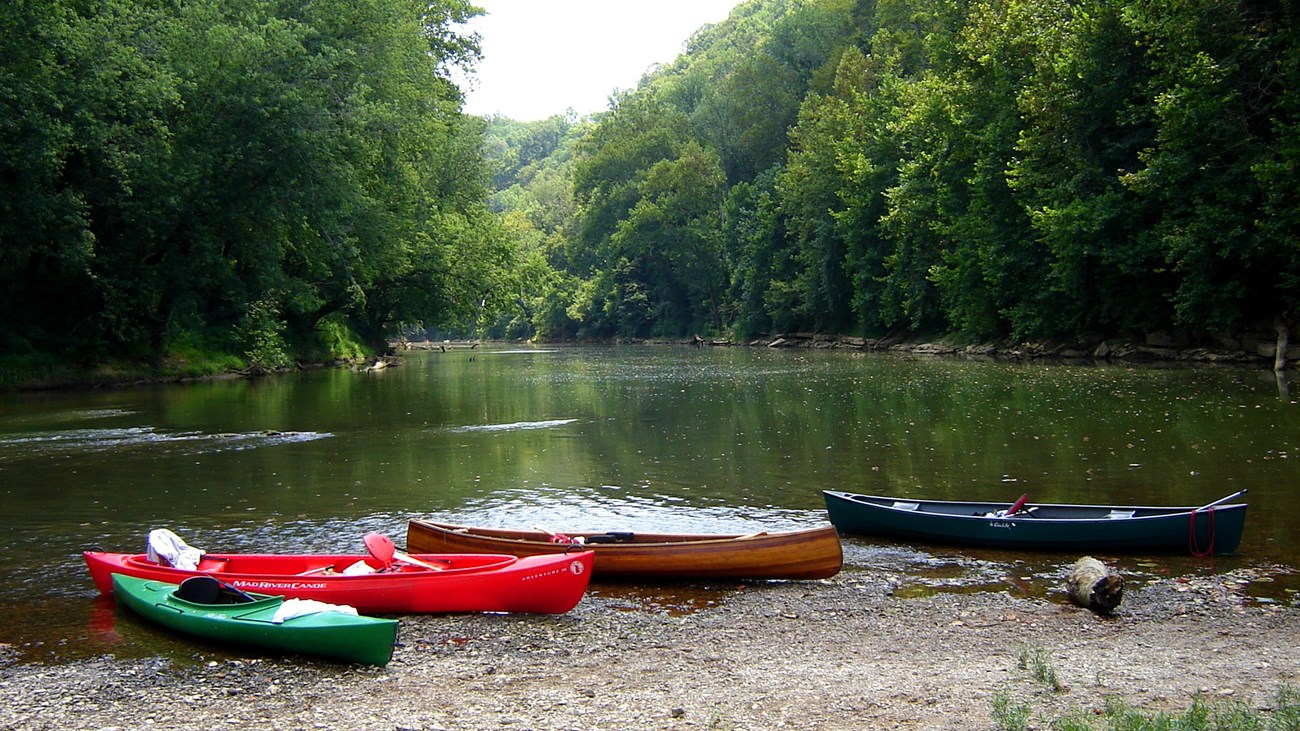 Canoes and kayaks sitting on the bank of a river.